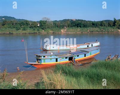 View across the Mekong River at Chiang Khong, Thailand, with Laos in the distance, and river boats on the near bank. Stock Photo