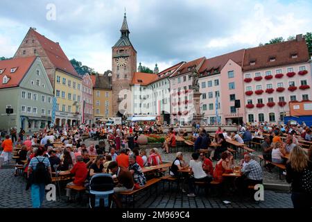 Weekend festival on the picturesque market square of Landsberg am Lech, Bavaria, Germany, with people sitting at trestle tables.  The Schoener Turm (Beautiful Tower), next to the old town hall, can be seen just left of centre in the background. Stock Photo