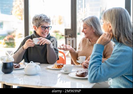 Group of elderly women having fun during breakfast in a cafeteria, three retired female friends are celebrating an anniversary, mature women drinking Stock Photo