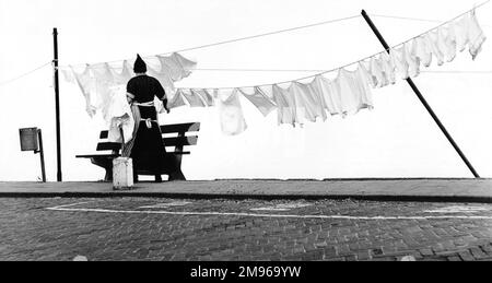 A woman hanging out the washing on a line (or two), apparently at the side of a stretch of water. Stock Photo