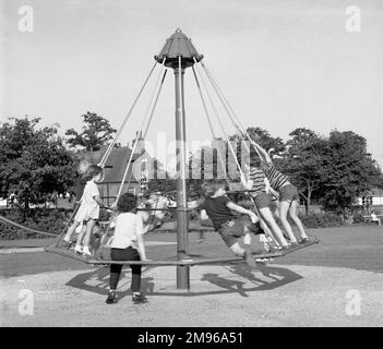 A group of children playing on an umbrella style roundabout on Lindfield Common, Sussex, England. Stock Photo