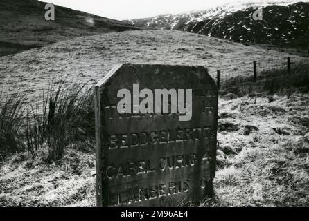 A fine example of an early 19th century slate milestone, standing by the roadside at Pen y Gwryd, near Llanberis, Caernarvonshire (now Gwynedd), North Wales.  A Roman camp stood on the rising ground just behind it, the Glyderau or Glyder range (Glyder Fach, Glyder Fawr and other peaks, part of the Snowdonia National Park) can be seen in the distance, and there is a mountain rescue post nearby. Stock Photo