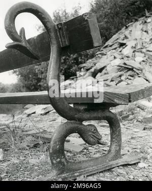 Close-up view of a municipal bench with a decorative iron dragon support, in the Nantlle Valley, North Wales.  A pile of slate waste indicates that the bench is not far from a closed-down slate quarry. Stock Photo