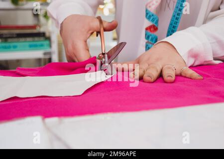 close-up of caucasian female hands cutting fabric with scissors on a table in a fashion clothing design workshop. Stock Photo