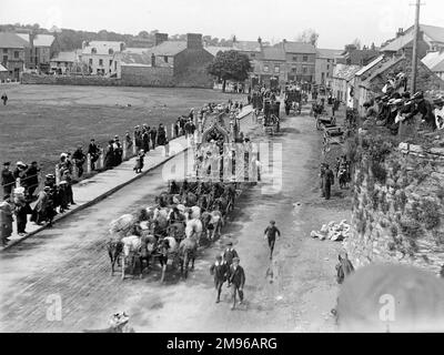 Street scene, showing part of Sanger's Circus parade during a visit to Haverfordwest, Pembrokeshire, Dyfed, South Wales, with several elaborate horse-drawn carriages, and riders dressed in fancy costumes.  People on the pavements stop and look, and a few boys follow in the roadway.  Some people are sitting on top of an old grass-covered limekiln (right).  Sanger was a famous circus impresario, staging spectacular shows at large venues all over the country from the 1850s onwards. Stock Photo