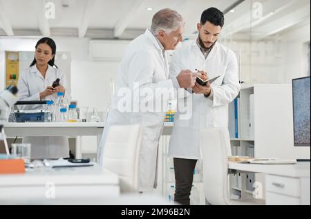 Always keep a detailed data record of every experiment. two scientists writing notes while having a discussion in a lab. Stock Photo