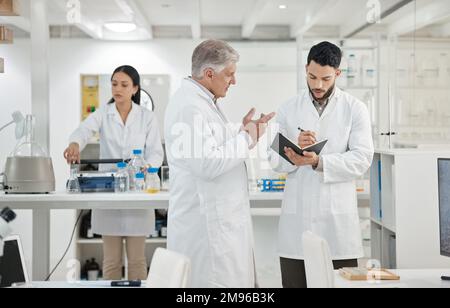 Id like you to set up the next experiment on your own. two scientists writing notes while having a discussion in a lab. Stock Photo