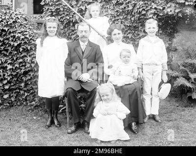 A middle class family (parents and five children) pose for their photo in a garden, probably in the Mid Wales area.  The little boy on the right is wearing a sailor suit. Stock Photo