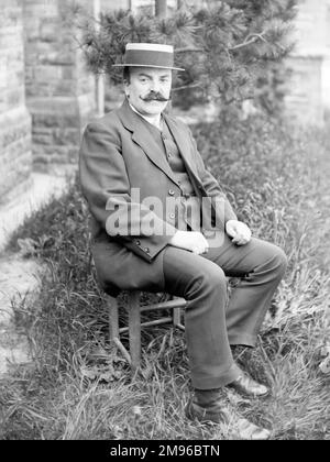 A smartly dressed middle aged Edwardian man poses for his photo in a garden, Mid Wales.  He is wearing a three-piece suit and a straw boater, and sits on a wooden chair on a slightly overgrown lawn. Stock Photo