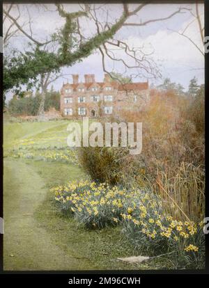 View of the gardens at Gravetye Manor, near East Grinstead, West Sussex, showing daffodils growing in the foreground, and the Elizabethan manor house in the background.  The gardens were developed by William Robinson, pioneer of the concept of the English Natural Garden, who lived at Gravetye from 1884 to 1935. Stock Photo