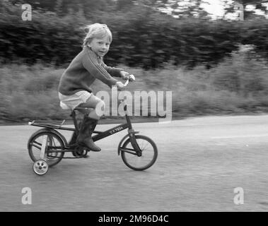 A little boy riding a bicycle with stabilisers on it. Stock Photo