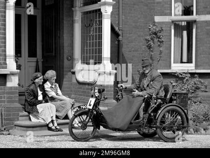 A man in a motorised bath chair in front of a house, with two women sitting on the doorstep clearly admiring his means of transport. Stock Photo