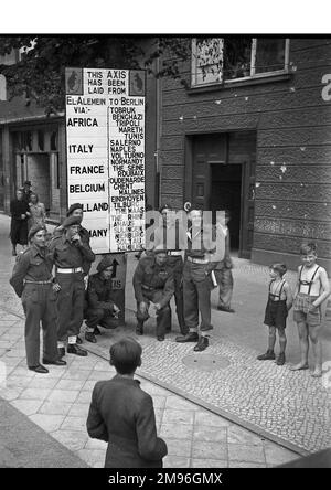 Street scene in Berlin, Germany, at the end of the Second World War, with soldiers and children.  A sign reads: This Axis has been laid from El Alamein to Berlin via Africa, Italy, France, Belgium, Holland, Germany, with various place names listed. Stock Photo