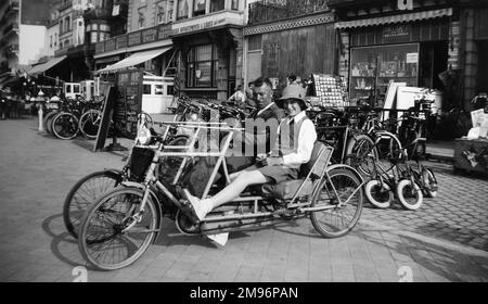 A couple on a four-wheeled two-seater cycle (also known as a velo double) outside the Taverne Emile in a town in Belgium. Stock Photo