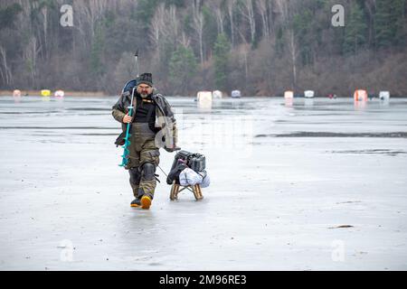 Fisherman fishing on a frozen lake in winter with fishing pole or rod, ice auger and equipment for fishing, portable thermal tents on background Stock Photo