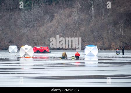 Fishermen fishing on a frozen lake in winter with fishing pole or rod, ice auger and equipment for fishing, portable thermal tents on background Stock Photo