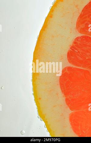 Close-up of fresh grapefruit slice on white background. Slice of red grapefruit in sparkling water on white background, close-up. Vertical image. Stock Photo