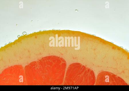 Slice of red grapefruit in water on white background. Grapefruit close-up in liquid with bubbles. Slice of red ripe grapefruit in water. Macro image o Stock Photo