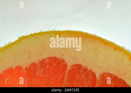 Slice of red grapefruit in water on white background. Grapefruit close-up in liquid with bubbles. Slice of red ripe grapefruit in water. Macro image o Stock Photo