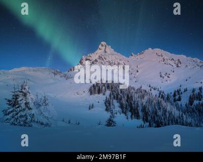 Aurora Borealis appear over a snow covered mountain in winter landscape. Northern lights mountain landscape Stock Photo
