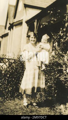 A mother smiles at the camera whilst holding her baby. Stock Photo