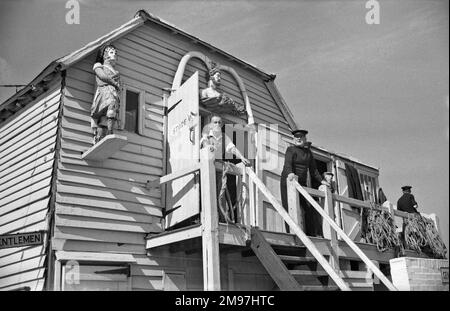 Men at a coastal storage hut with figureheads from ships on display. Stock Photo