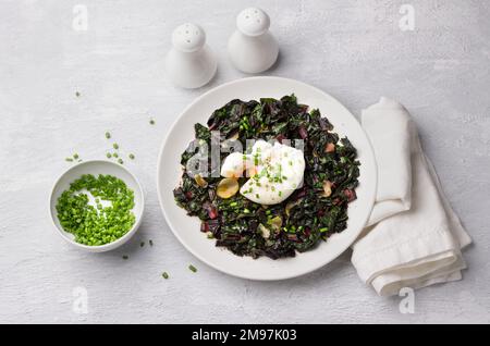Braised chard with garlic and poached egg, seasoned with spices and green onions on gray background, top view. delicious healthy breakfast Stock Photo