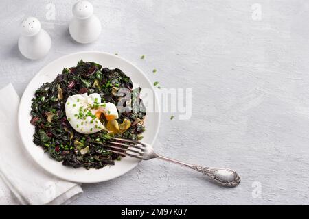 Braised chard with garlic and poached egg, seasoned with spices and green onions on gray background, top view, free space. delicious healthy breakfast Stock Photo