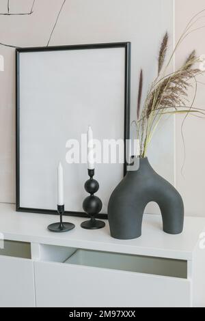 Modern ceramic vase with two candlesticks and an empty picture frame on a sideboard Stock Photo