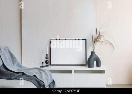 Modern ceramic vase with two candlesticks and an empty picture frame on a sideboard next to a sofa Stock Photo