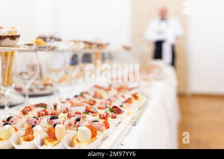 Various canapes appetizers served on buffet table. Waiter in the background. Stock Photo