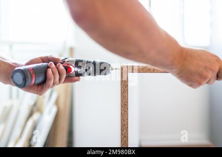 Close up of worker installing kitchen shelf by using cordless screwdriver at home. Space for copy. Stock Photo