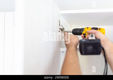 Handyman using screwdriver while installing kitchen cabinets at home Stock Photo