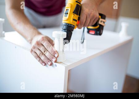Man installing new furniture at his home and using cordless screwdriver Stock Photo