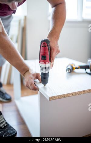 Man installing wooden shelves by using cordless screwdriver Stock Photo