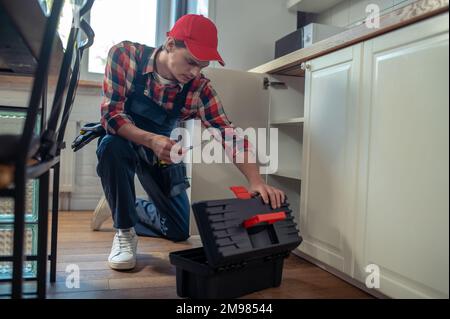 Calm focused repairman with a screwdriver in the hand looking into the open plastic toolbox Stock Photo