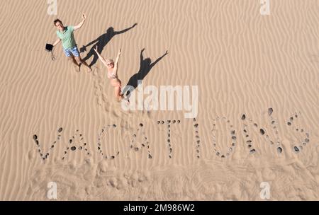 Overhead view of a man and woman standing in sand dunes next to the word vacations, Maspalomas, Gran Canaria, Canary Islands, Spain Stock Photo