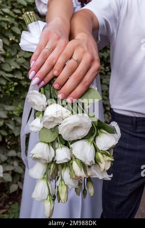 Hands of newlyweds with rings on a bouquet of flowers close-up. Husband and wife keep their hands with wedding rings Stock Photo
