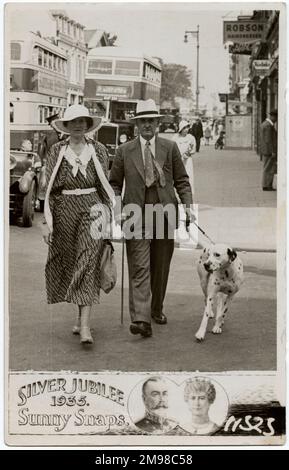 Smart Couple with their lovely pet Dalmatian walking along the pavement. Sunny Snaps operated in a number of different locations (often on the south coast), taking 'walking pictures', which they would then sell to the subjects! This photograph dates from the year (1935) of the Silver Jubilee of King George V and Queen Mary. The best Dalmatian dogs (as pictured here) have no spots on their tails! Stock Photo