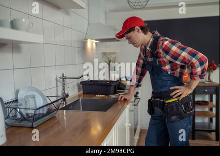 Side view of a serious concentrated plumber inspecting the water tap in the customer kitchen Stock Photo
