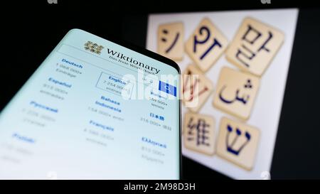Mobile phone with webpage of online dictionary Wiktionary (Wikimedia) on screen in front of logo. Focus on top-left of phone display. Stock Photo