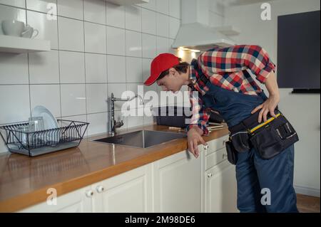 Expert plumbing technician carrying out the inspection of the water faucet in the client kitchen Stock Photo