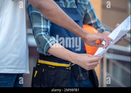 Cropped photo of a customer pointing at a rolled-out technical drawing in the engineer hands Stock Photo