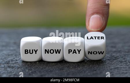 Hand turns dice and changes the expression 'buy now pay now' to 'buy now pay later'. Stock Photo