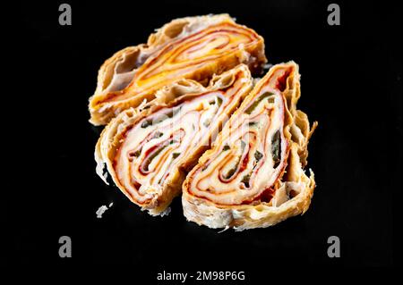 Three piece of sliced salty rolled pastry with ham, cheese and jalapenos on black background, closeup. Nice layers of food on the cut. Appetizer, snac Stock Photo