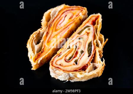 Two piece of sliced salty rolled pastry with ham, cheese and jalapenos on black background, closeup. Stock Photo