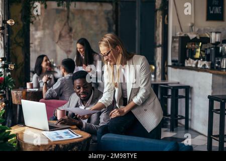 Young woman shows documents to her colleague as he drinks coffee in cafe. Stock Photo