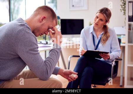 Woman Doctor Or GP In Office Meeting Young Male Patient With Poor Mental Health For Appointment Stock Photo