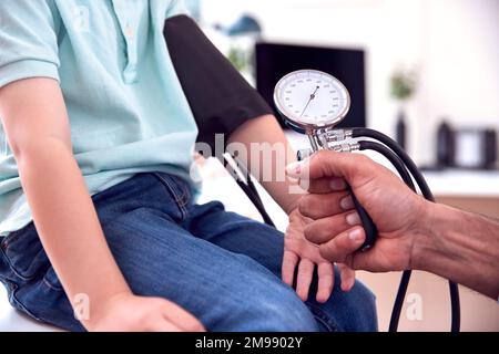 Close Up Of Male Doctor Or GP Examining Boy Taking Blood Pressure With Sphygmomanometer Stock Photo