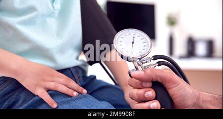 Close Up Of Male Doctor Or GP Examining Boy Taking Blood Pressure With Sphygmomanometer Stock Photo